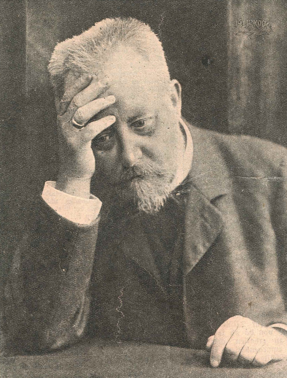 Foto eines Mannes mit Bart, mit der rechten Hand seinen an der Stirn den Kopf aufstützend