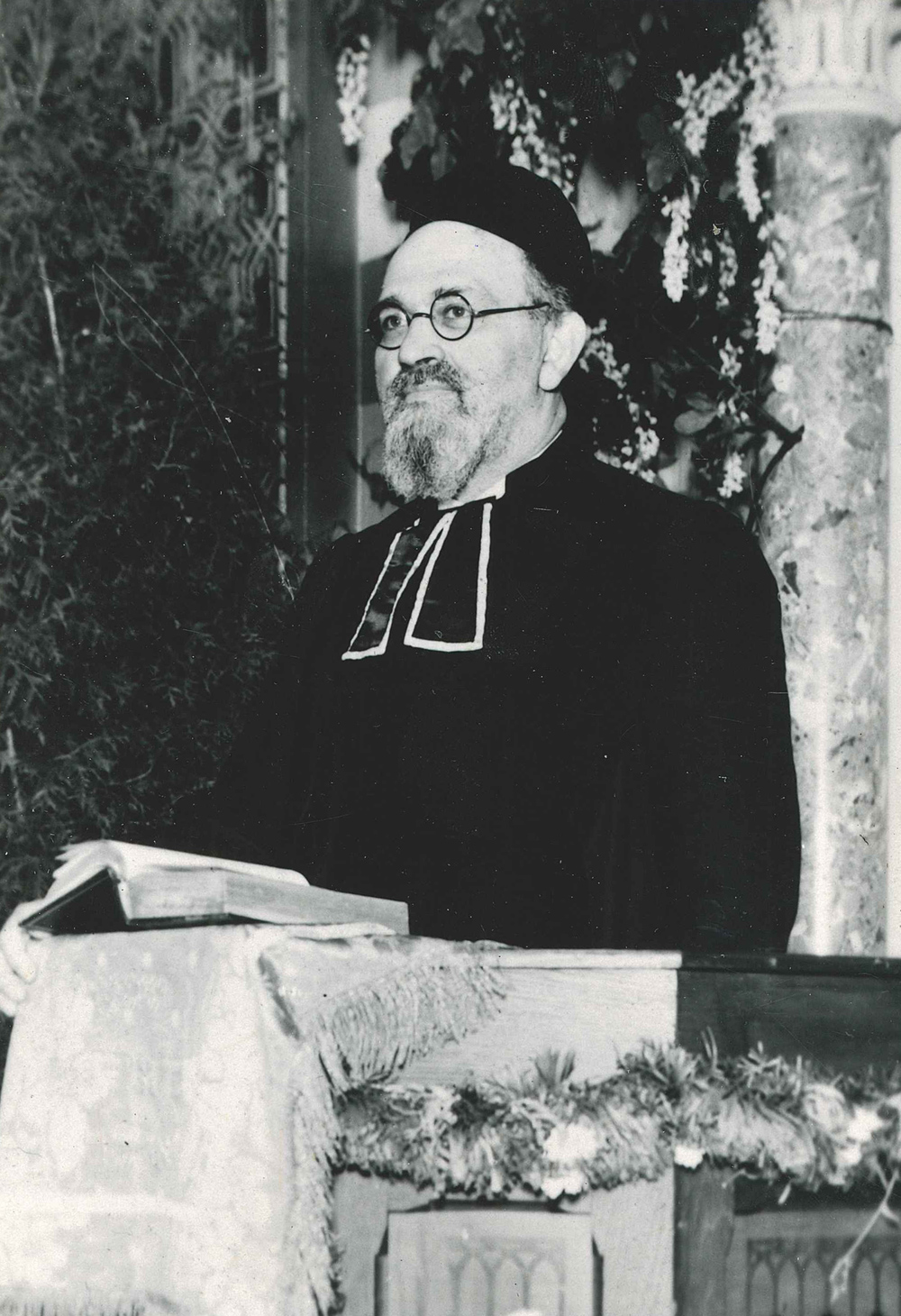 Rabbiner mit Nickelbrille steht in der Bima (Vorlesepult)