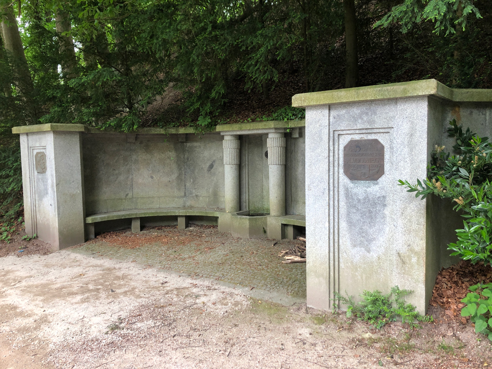Brunnen mit Gedächtnisplatte und Bildnis sowie Bänken